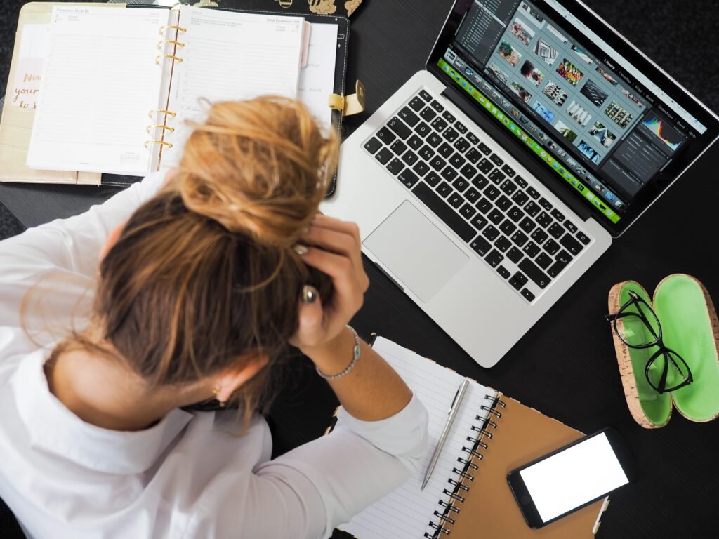 Meditation For Busy Mind. A woman sits in front of a laptop with her head in her hands.